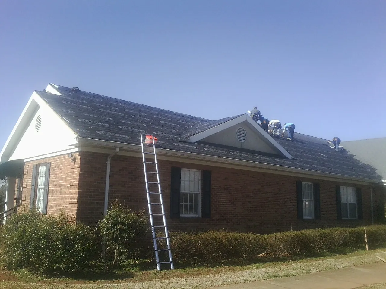 Crew tearing shingles off a brick ranch roof with a ladder set — Metal Roof Repair work by our crew in Richland