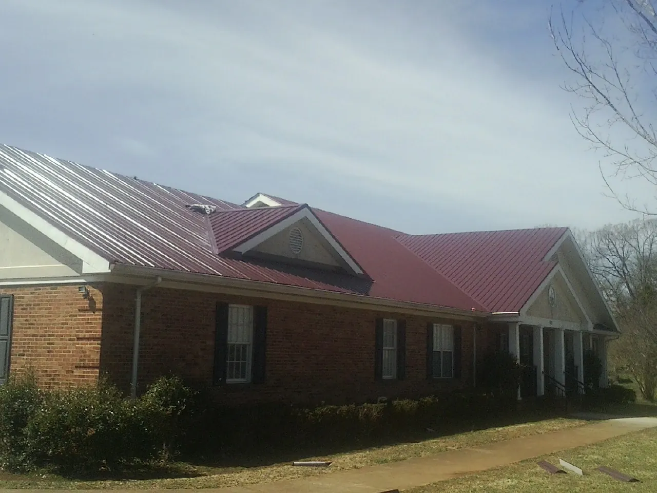 Red metal roof with gabled entries on a long brick building, from a Hail Damage Roof Repair job in Richland
