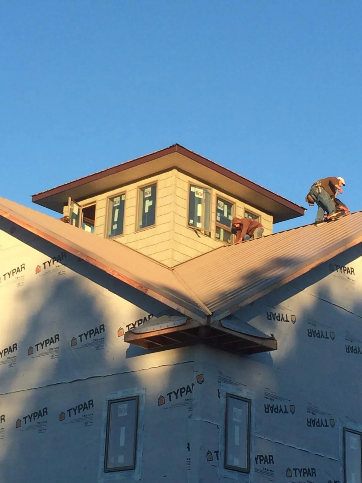 Roofers working around a rooftop cupola on a new metal roof at sunset in Richland